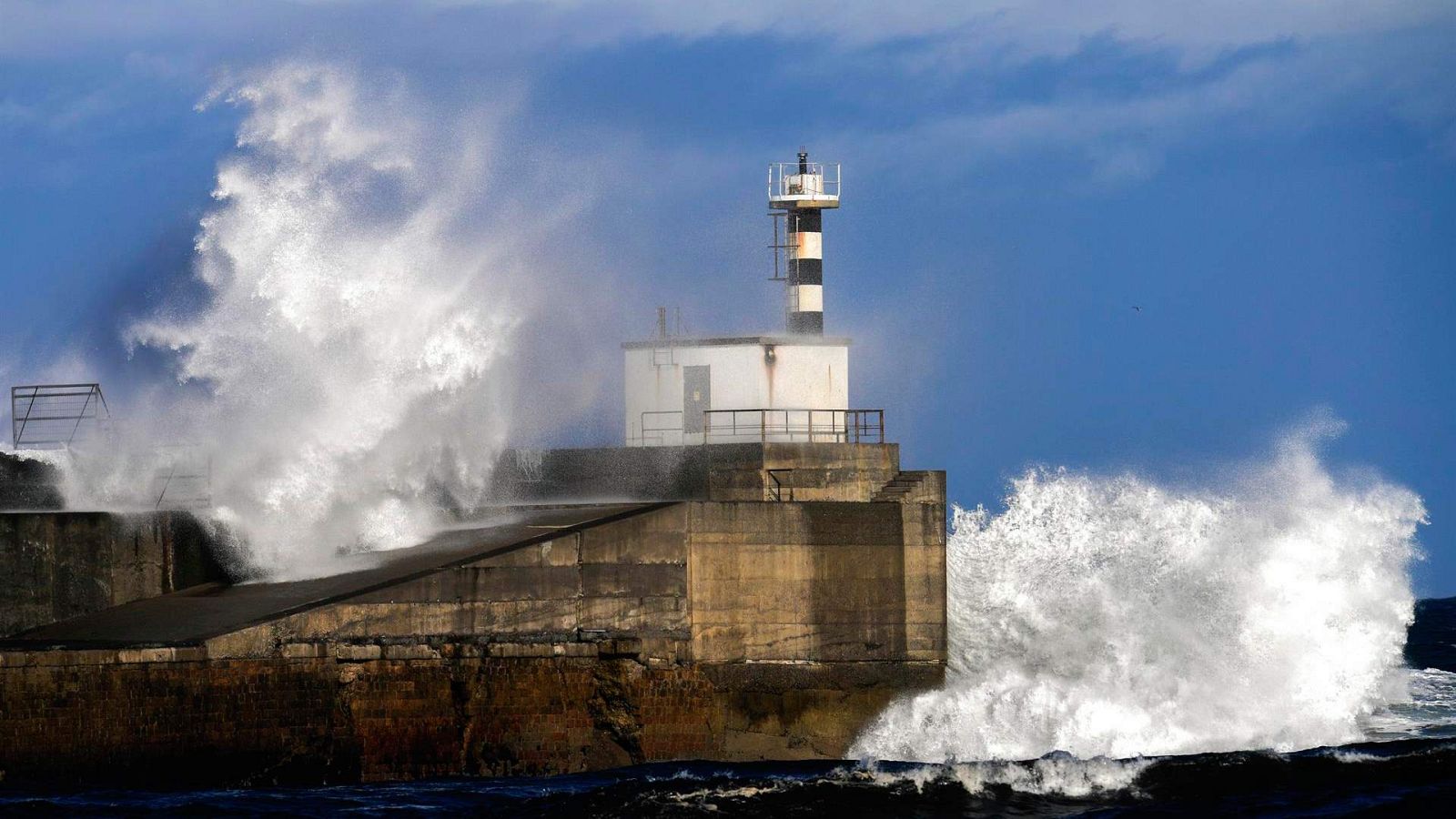 Olas de gran tamaño rompen contra el faro del puerto de San Esteban en Muros de Nalón, en Asturias.