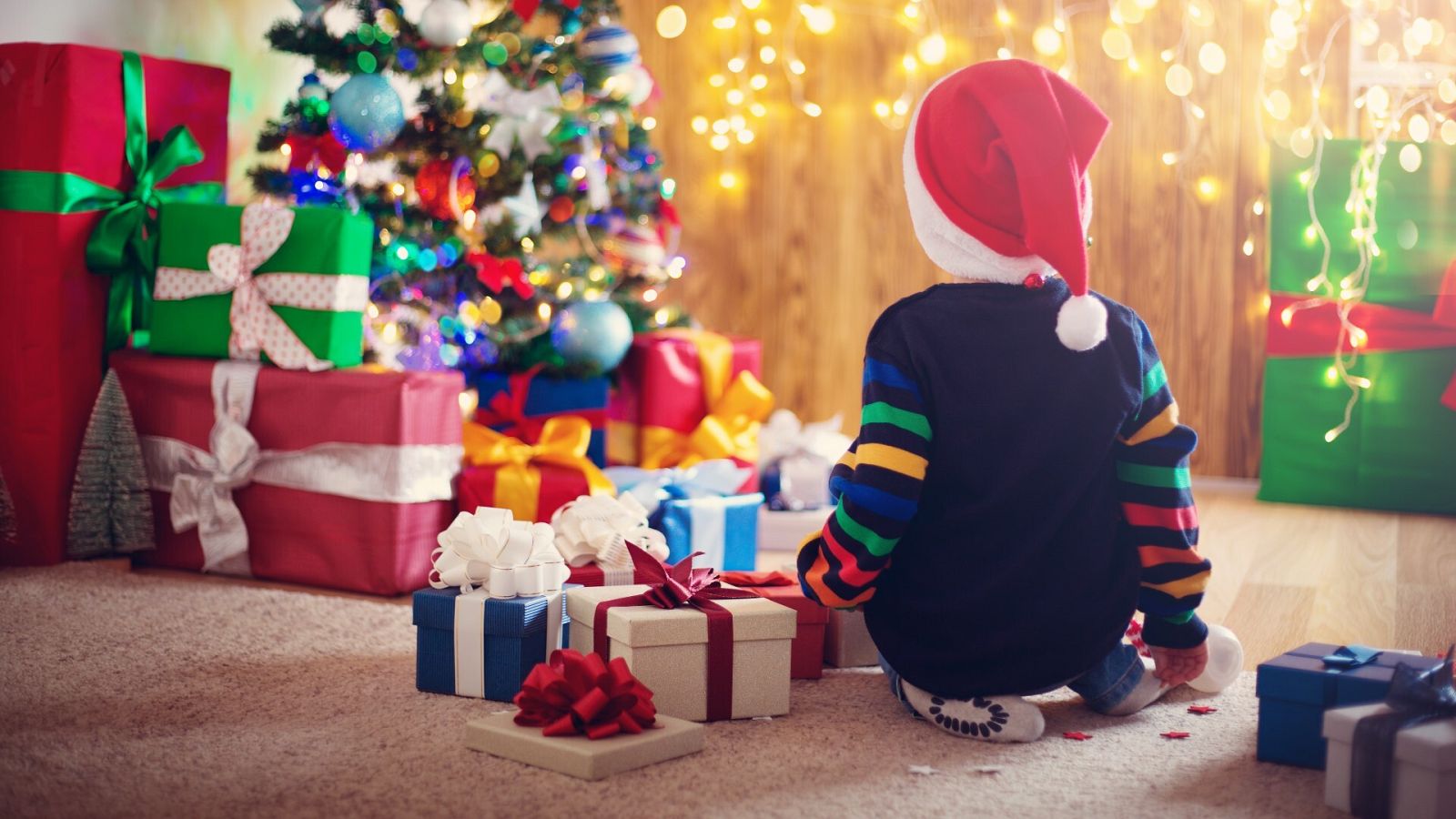 Un niño con un gorro de Navidad junto a un montón de regalos