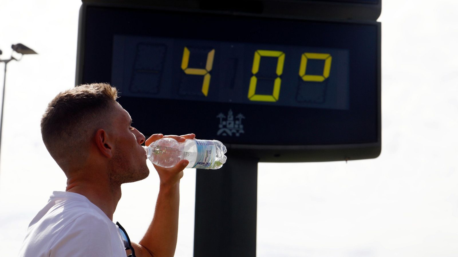 Un joven bebe agua junto a un termómetro de calle que marca 40 grados en el centro de Córdoba a finales de abril de 2023