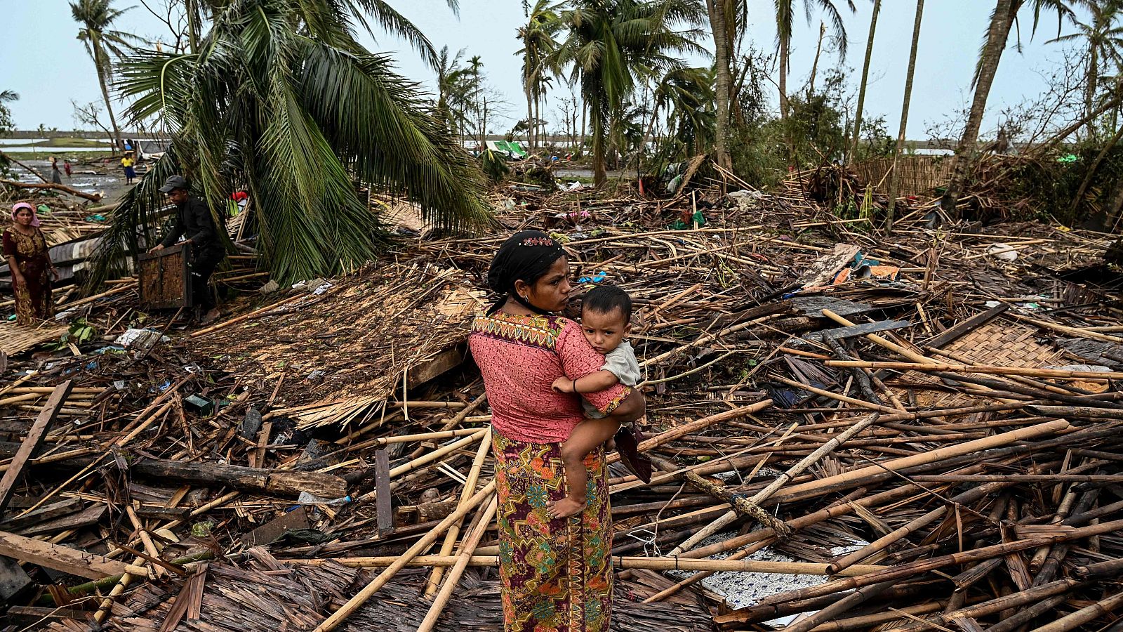 Una mujer rohingya lleva a su bebé junto a su casa destruida en el campo de refugiados de Basara, en Sittwe