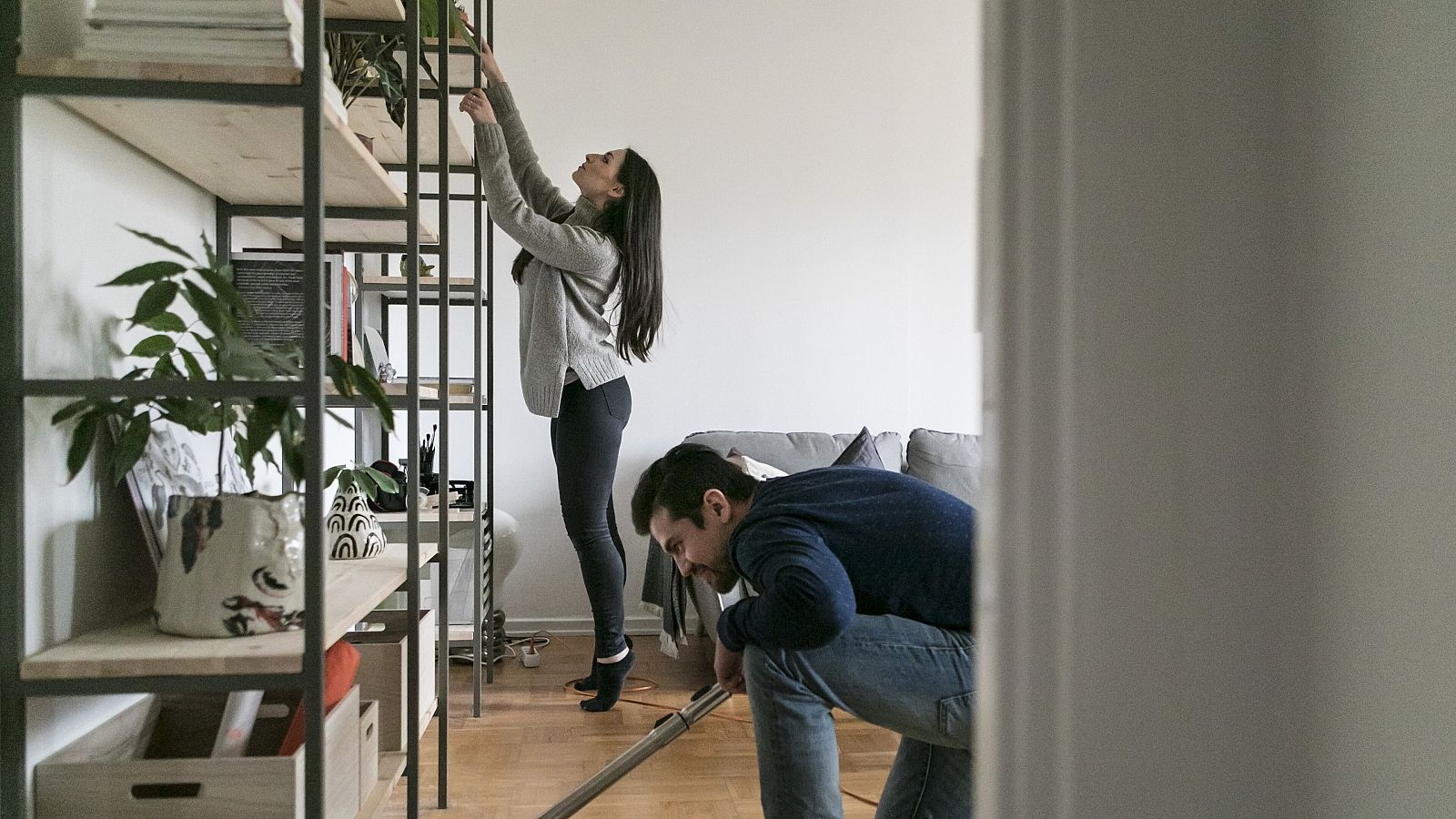 Un hombre aspira el suelo mientras una mujer limpia una estantería en casa