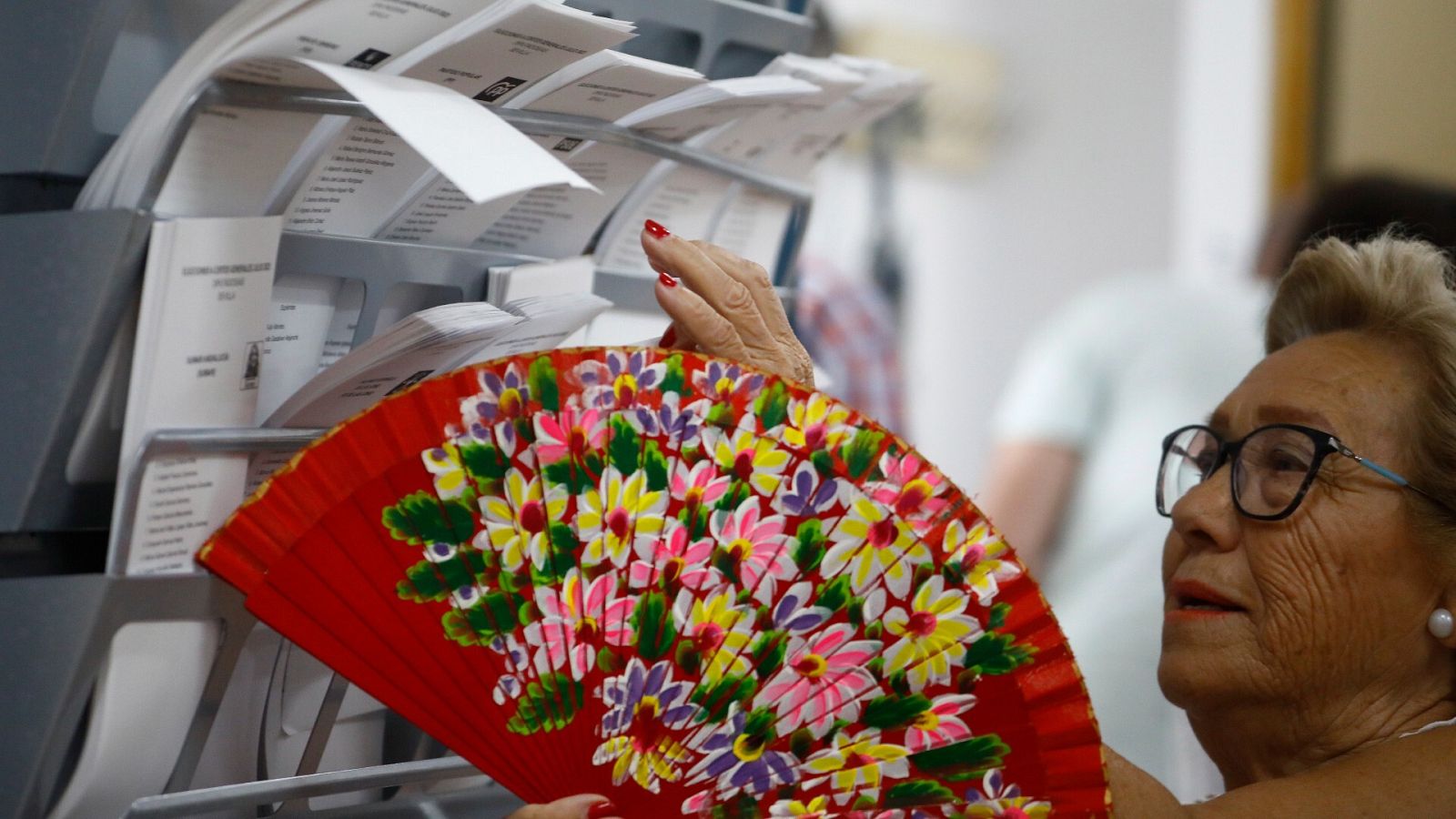 Una mujer con abanico elige una papeleta para el 23J
