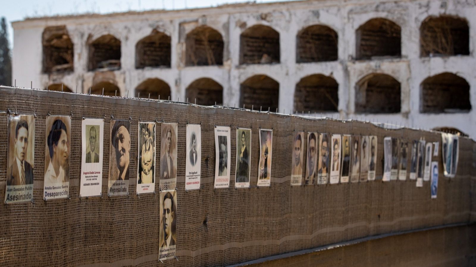 Fotos de personas desaparecidas en la valla para proteger los trabajos de exhumación de la fosa común de Pico Reja