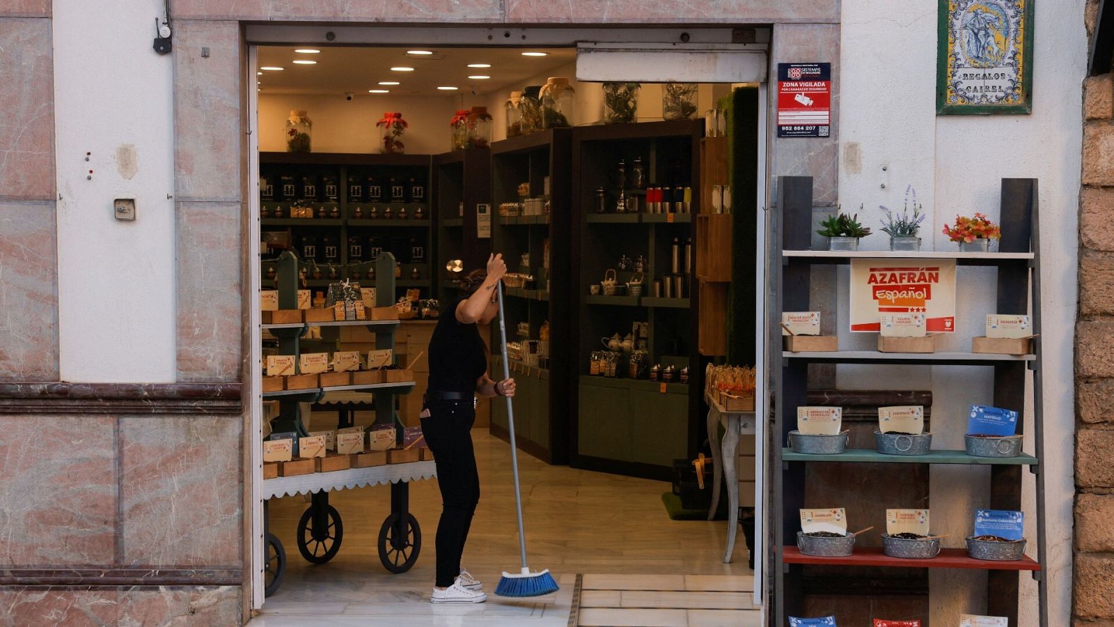 Una mujer barre la entrada de un pequeño comercio