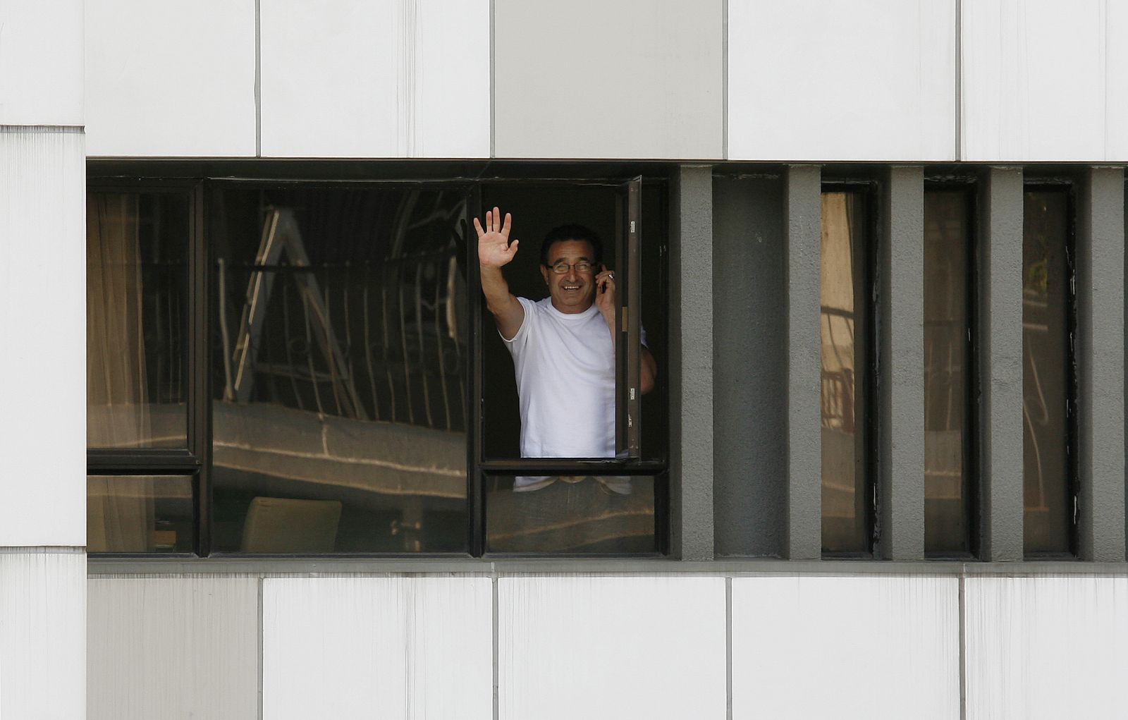A hotel guest who is confined to his room waves to journalists as he talks on a mobile phone in Hong Kong
