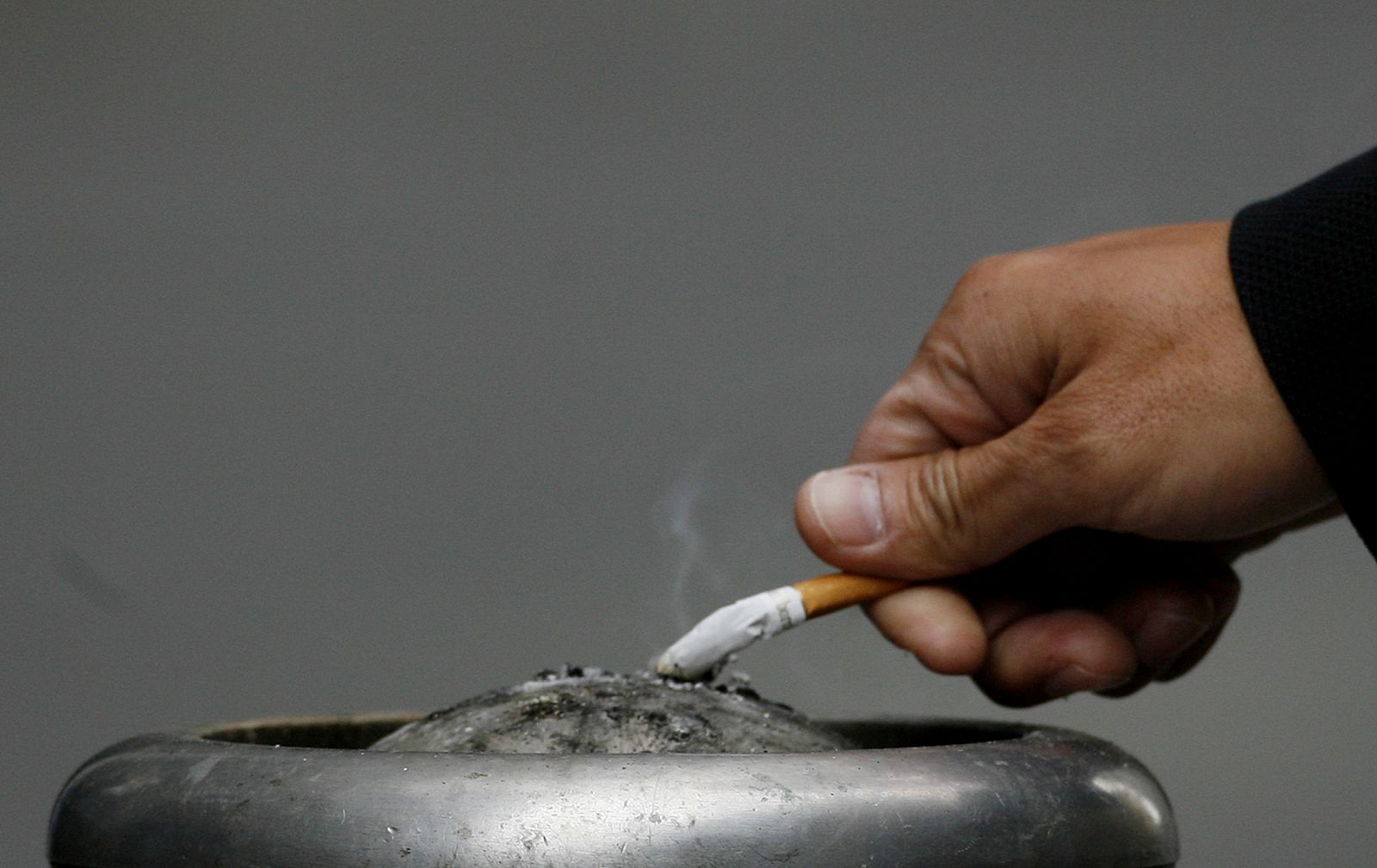 Un hombre apaga su cigarrillo en un cenicero