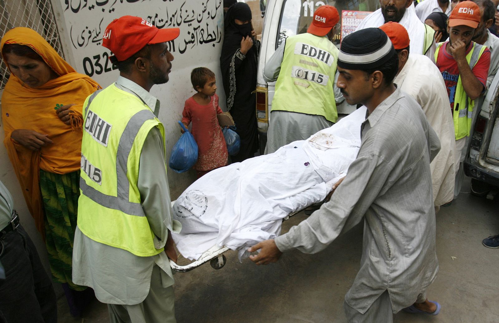 Rescue workers carry the body of a woman, who perished in a stampede while collecting food items, out of a morgue for burial in Karachi