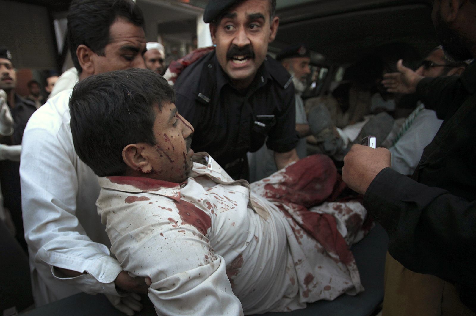 A policeman and volunteers assist a man, who was injured by a suicide bomb blast in Charsadda, at a hospital in Peshawar