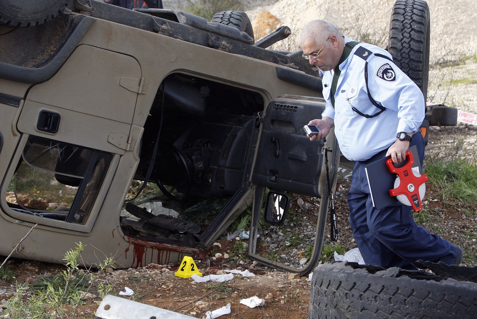 An Israeli police officer walks near an overturned army vehicle with blood on it near  Nablus