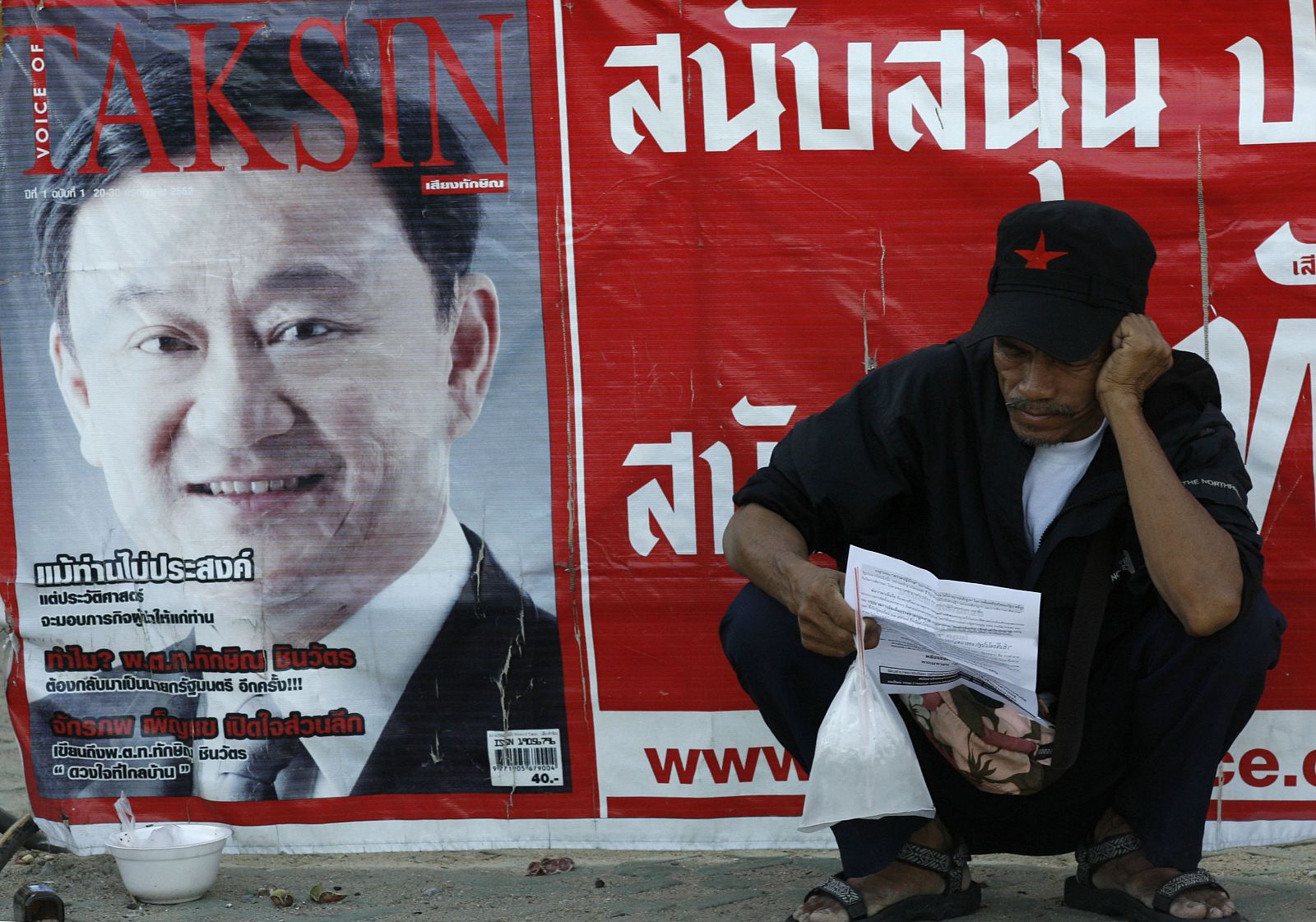 A supporter of former Thai prime minister Thaksin Shinawatra sits next to Thaksin's campaign banner at Sanam Luang