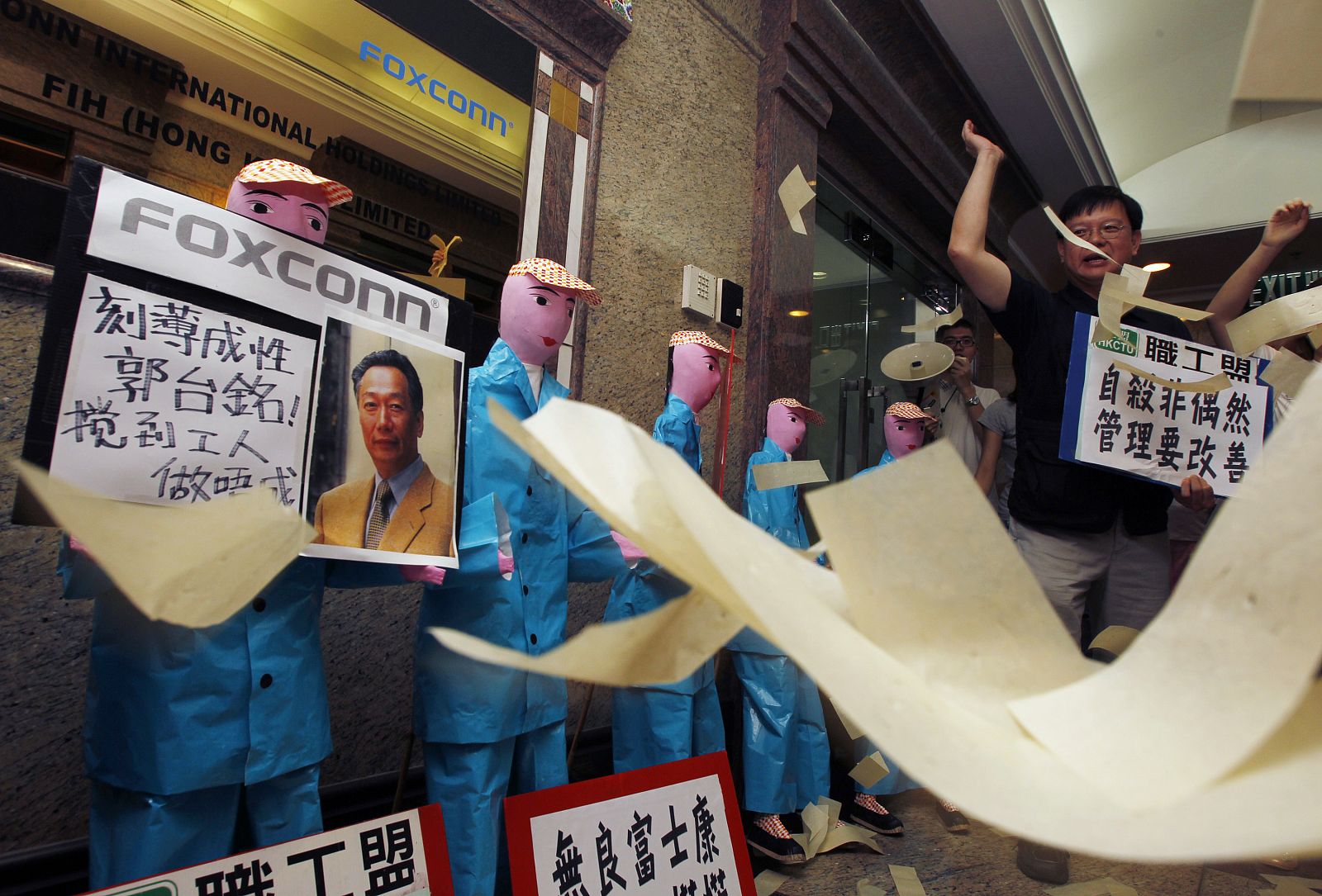 Protesters throw paper money in front of paper figures, depicting workers who recently died in apparent suicides, during a traditional Chinese mourning ceremony outside a Foxconn office in Hong Kong