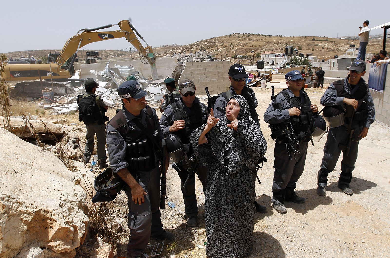A Palestinian woman gestures in front of Israeli police officers as the home of her neighbours is razed in East Jerusalem