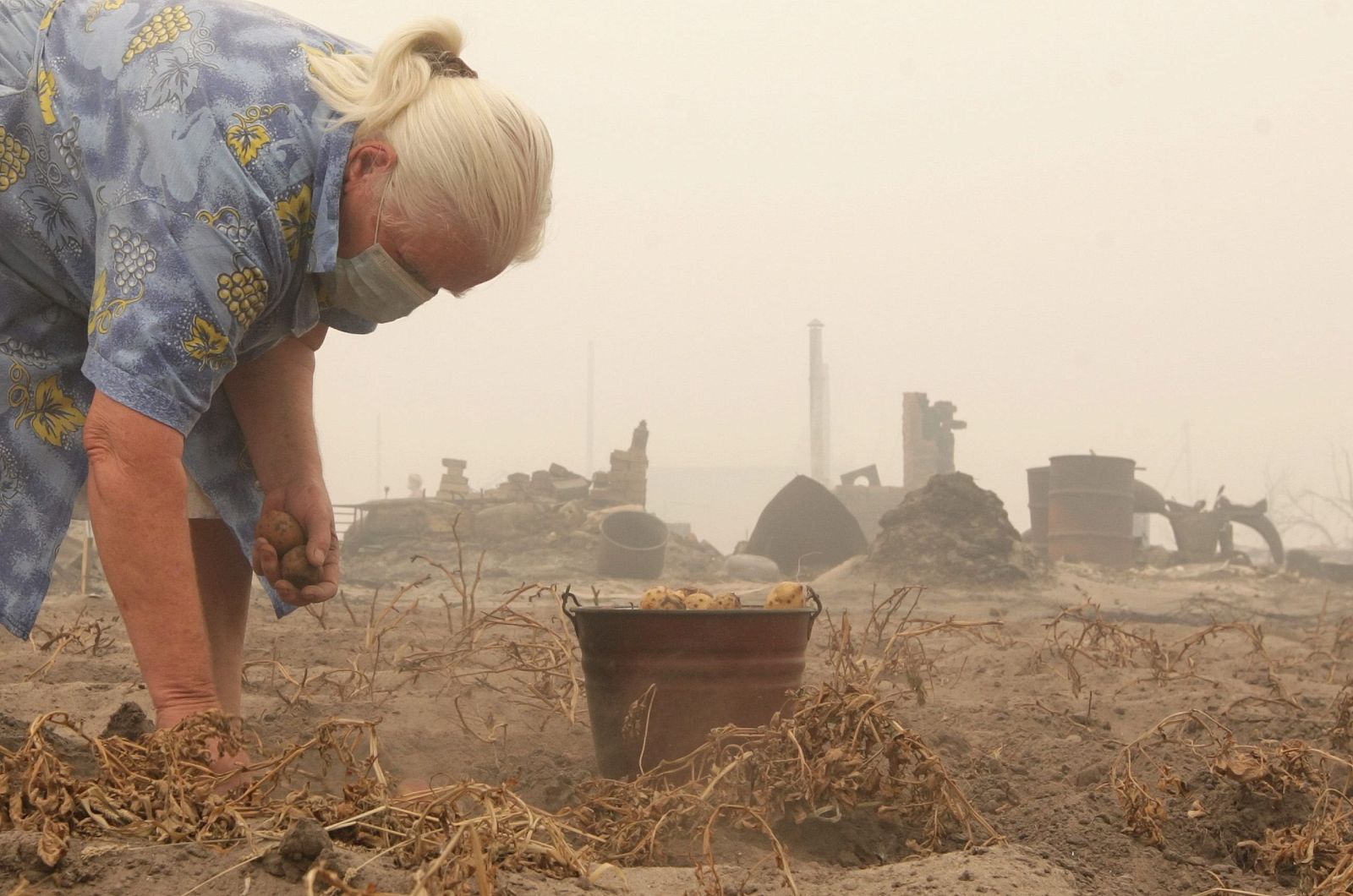 Una mujer recoge patatas con una mascarilla junto a una casa quemada en la localidad rusa de Laskovo, en la región de Ryazan.