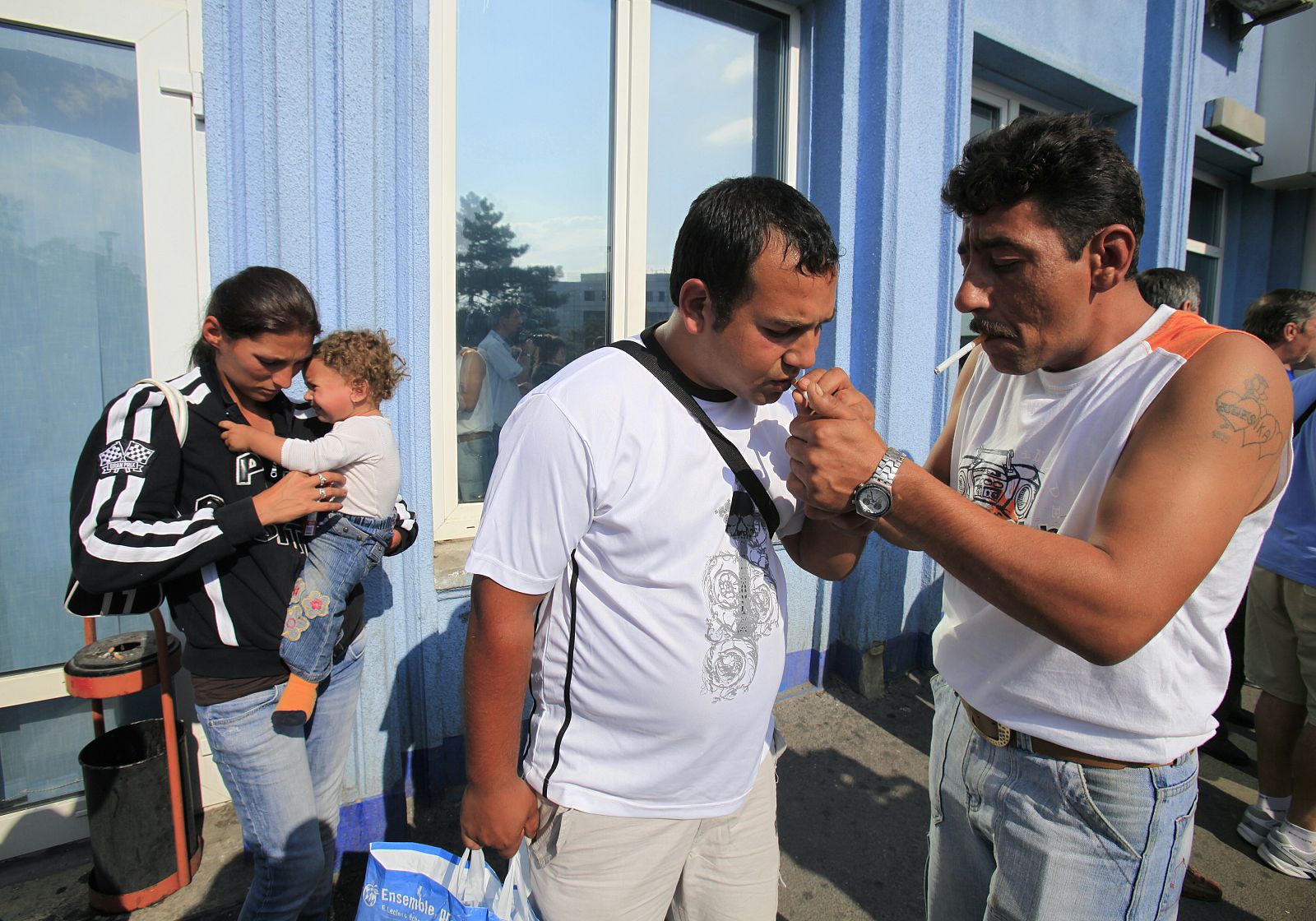Putzi lights a cigarette for another Roma after arriving with his family on a voluntary repatriation scheme from France in Bucharest