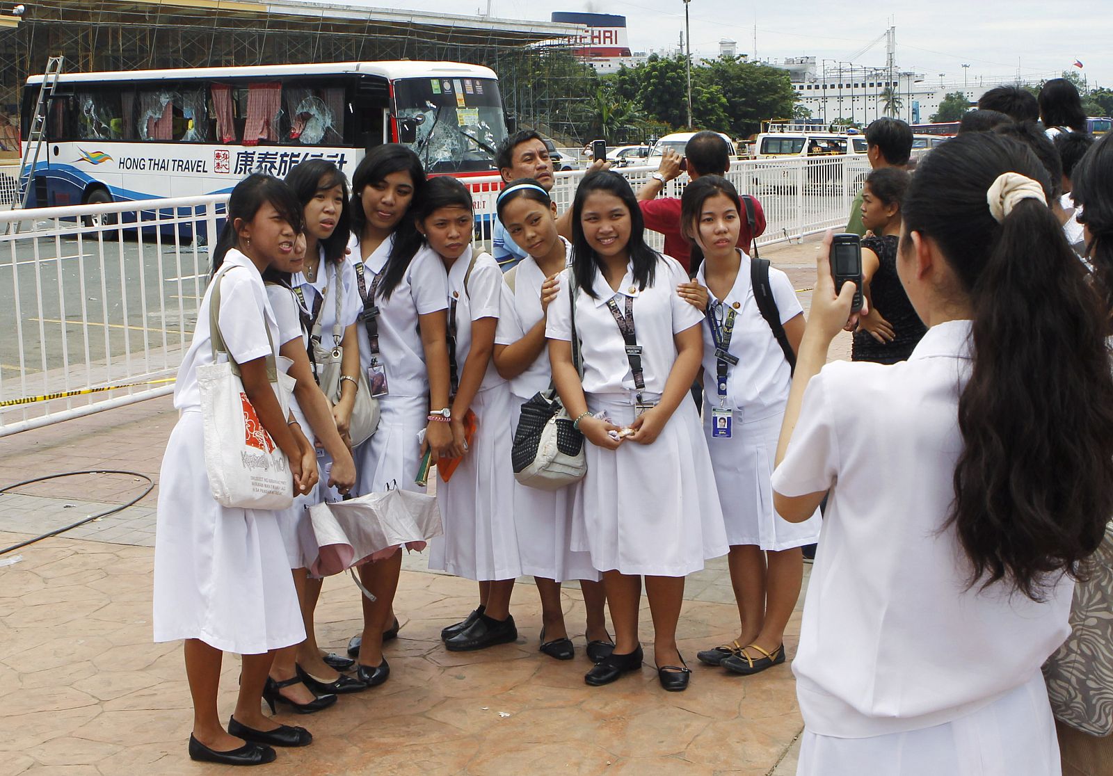 Students pose for photographs near the damaged tourist bus involved in a hostage crisis in Manila