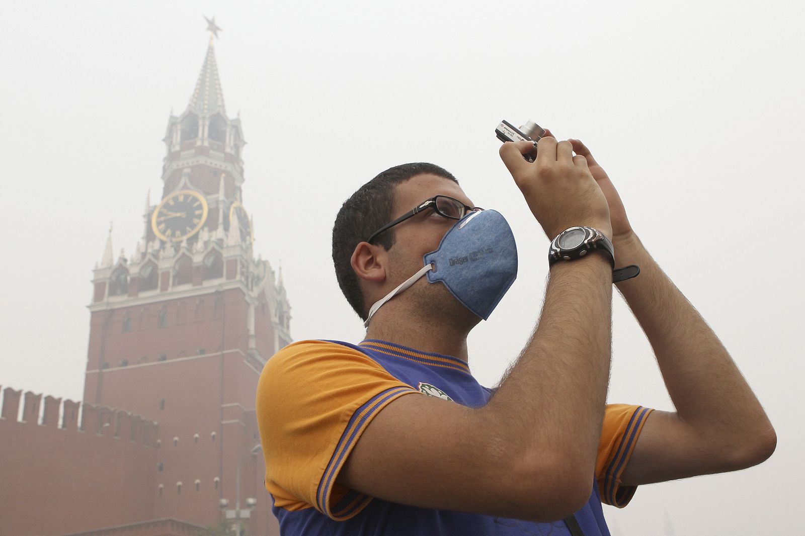 A tourist, wearing a mask to protect himself from the smell of heavy smog caused by peat fires in nearby forests, takes a picture as he walks along Red Square in central Moscow