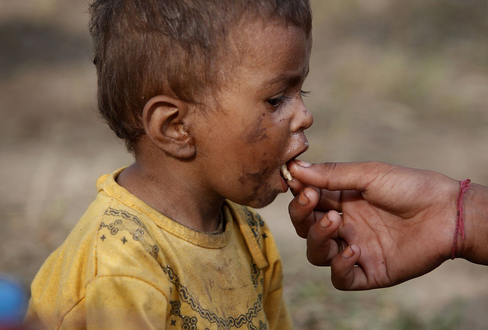 A two-year-old flood victim is fed by his sister as they take refuge with his family in a public park in Thatta