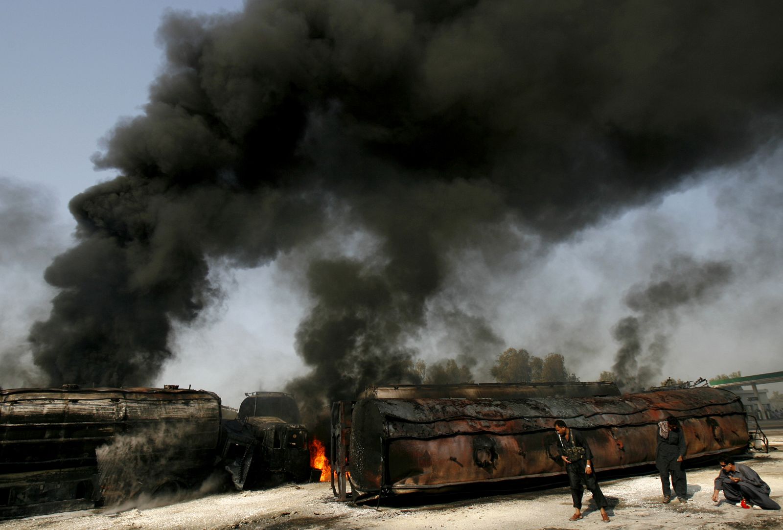 Police collect bullets shells next to burning oil tankers on a highway near Shikarpur