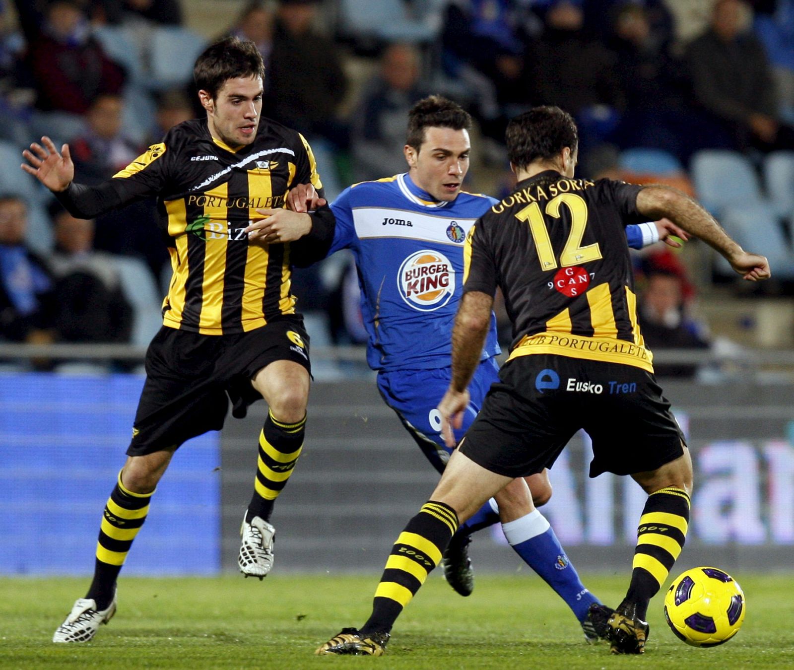 El delantero del Getafe Adrián Colunga lucha un balón con los jugadores del Portugalete, Otiñano (i) y Gorka.