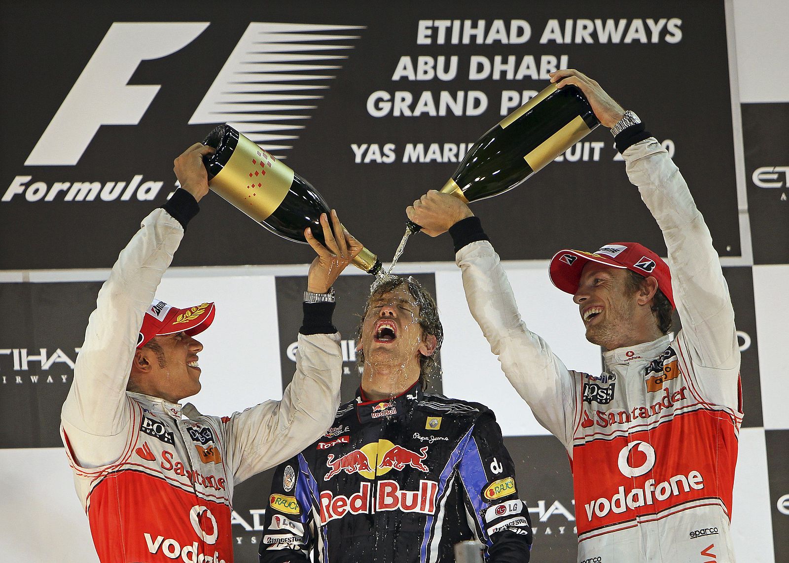 Los pilotos británicos de McLaren Mercedes, Lewis Hamilton y Jenson Button echan champán al alemán de Red Bull, Sebastian Vettel, campeón en Abu Dabi y del Mundial 2010.