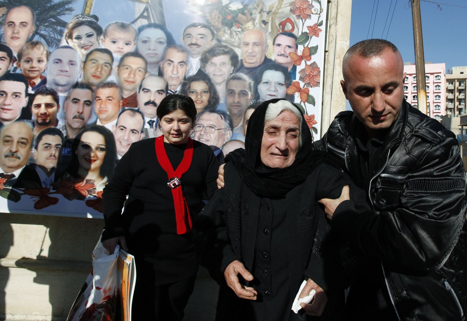 People grieve near a mural with pictures of victims killed in the October 31 attack on Our Lady of Salvation Church by gunmen, after a Christmas mass in Baghdad