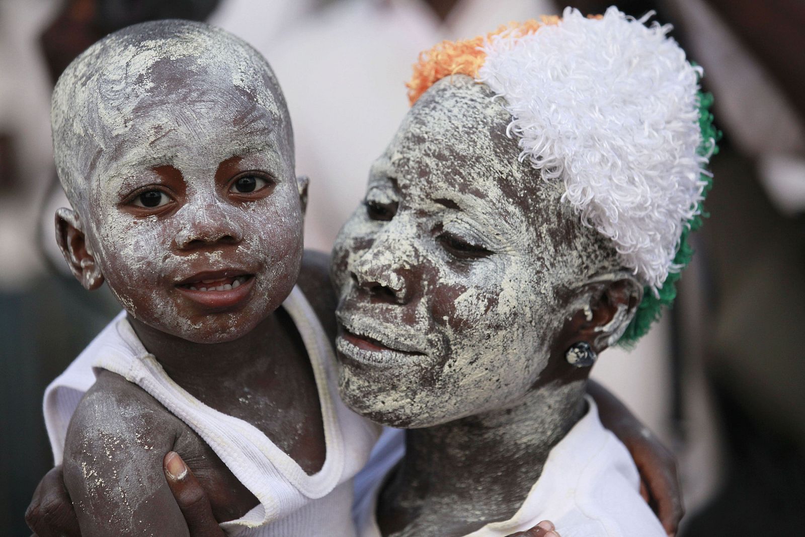 A supporter of Ivory Coast's incumbent leader Laurent Gbagbo carries her child, both with clay powder on their faces, during a rally in Abidjan