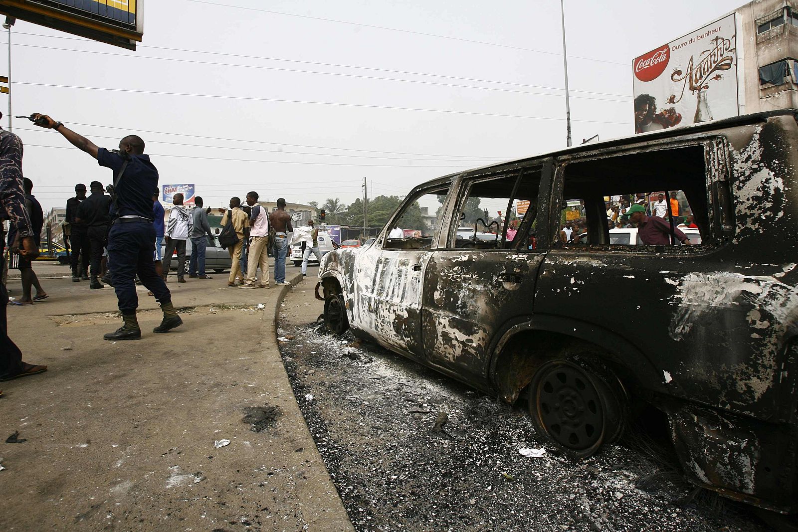 A police officer stands near an U.N. vehicle which was burnt during a protest by students at the junction of Riviera 2 in Abidjan