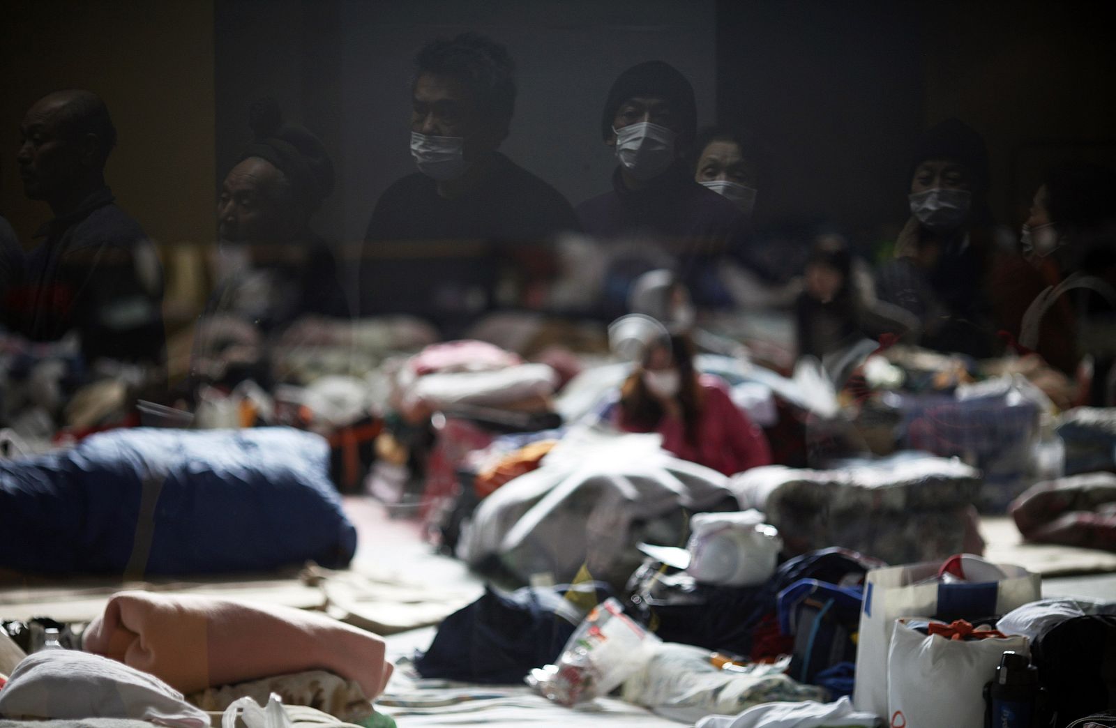 Earthquake and tsunami survivors are reflected in the window of a collective shelter as they wait for food to be distributed in Kesennuma