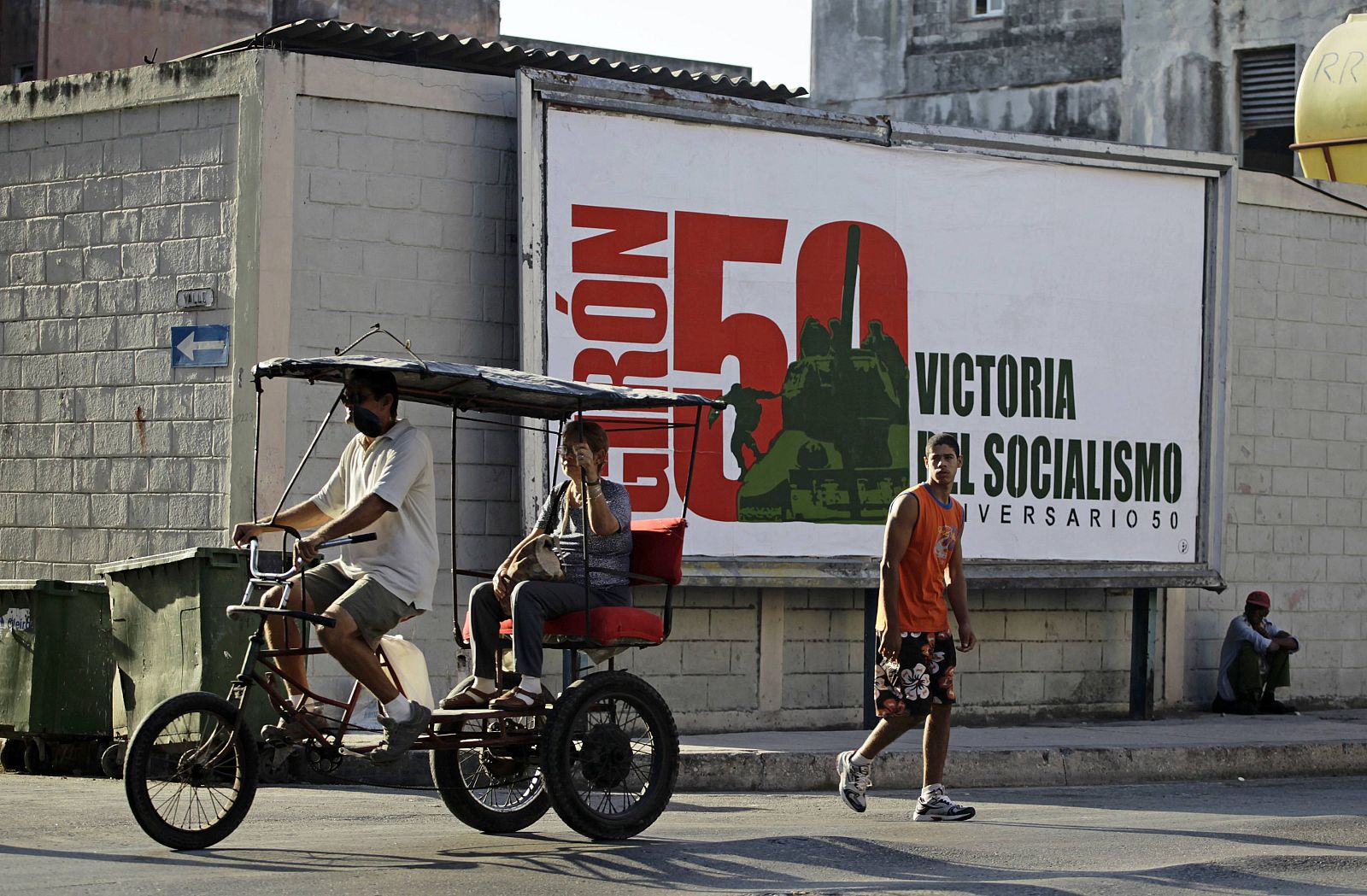 A man carries a woman on his tricycle taxi beside a billboard celebrating the 50th anniversary of "Giron", the U.S.-backed Bay of Pigs invasion, with a 1961 image of former leader Fidel Castro jumping off a tank in Havana