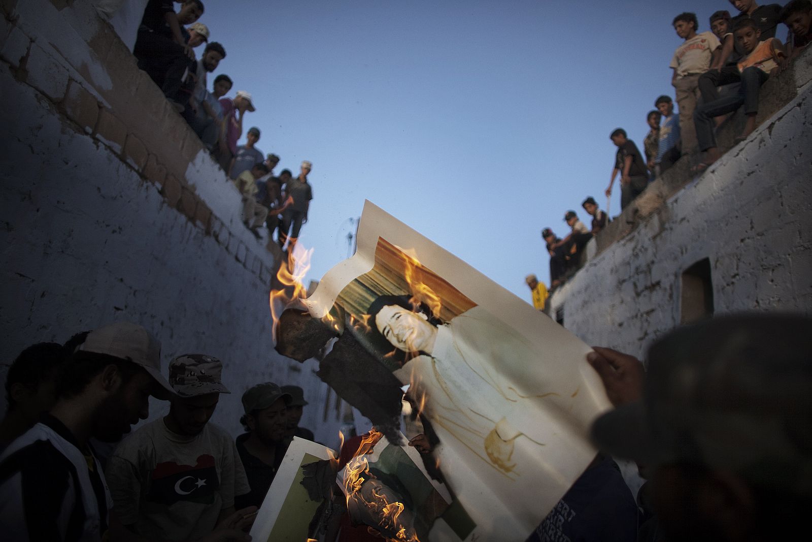 Un grupo de jóvenes libios miran a manifestantes quemando un retrato de Gadafi