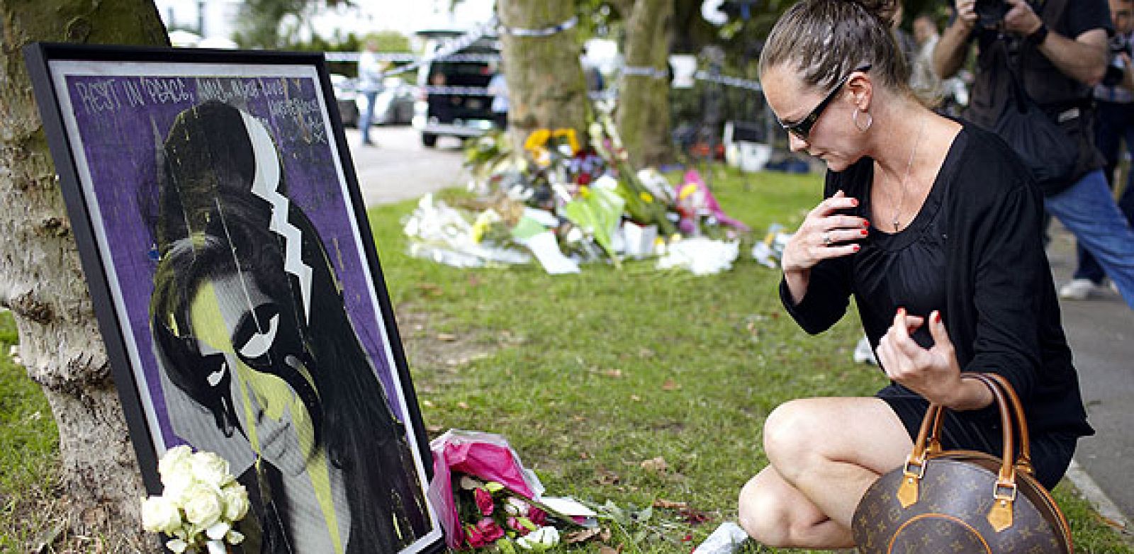 Una mujer ofrece sus respetos ante los ramos de flores que han sido colocados frente a la casa de la fallecida cantante Amy Winehouse