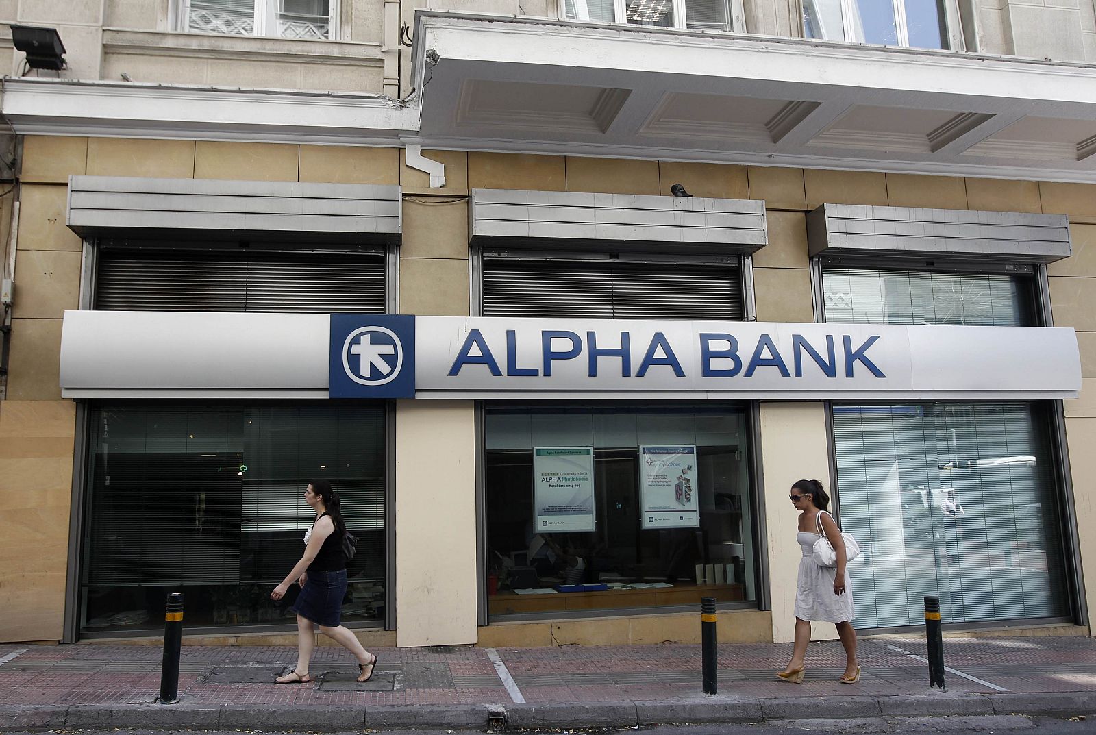 Women walk outside an Alpha bank branch in Athens