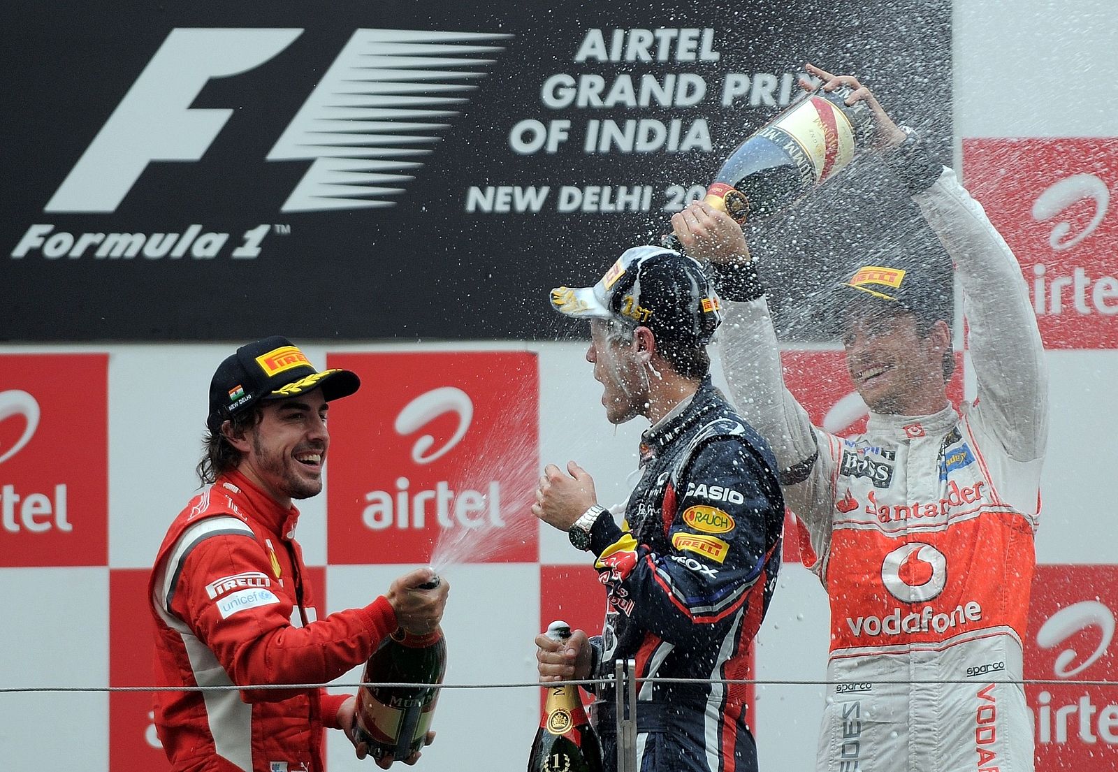 Fernando Alonso (i) y Jenson Button (d) rocían con champagne a Sebastian Vettel (c) tras ganar el GP de India.