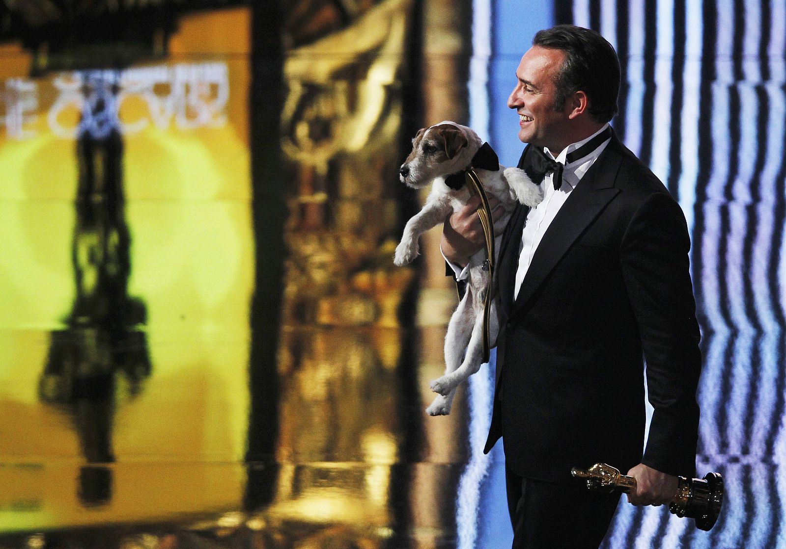 Best actor winner Dujardin of France carries Uggie the dog after "The Artist" won the Oscar for Best Picture at the 84th Academy Awards in Hollywood