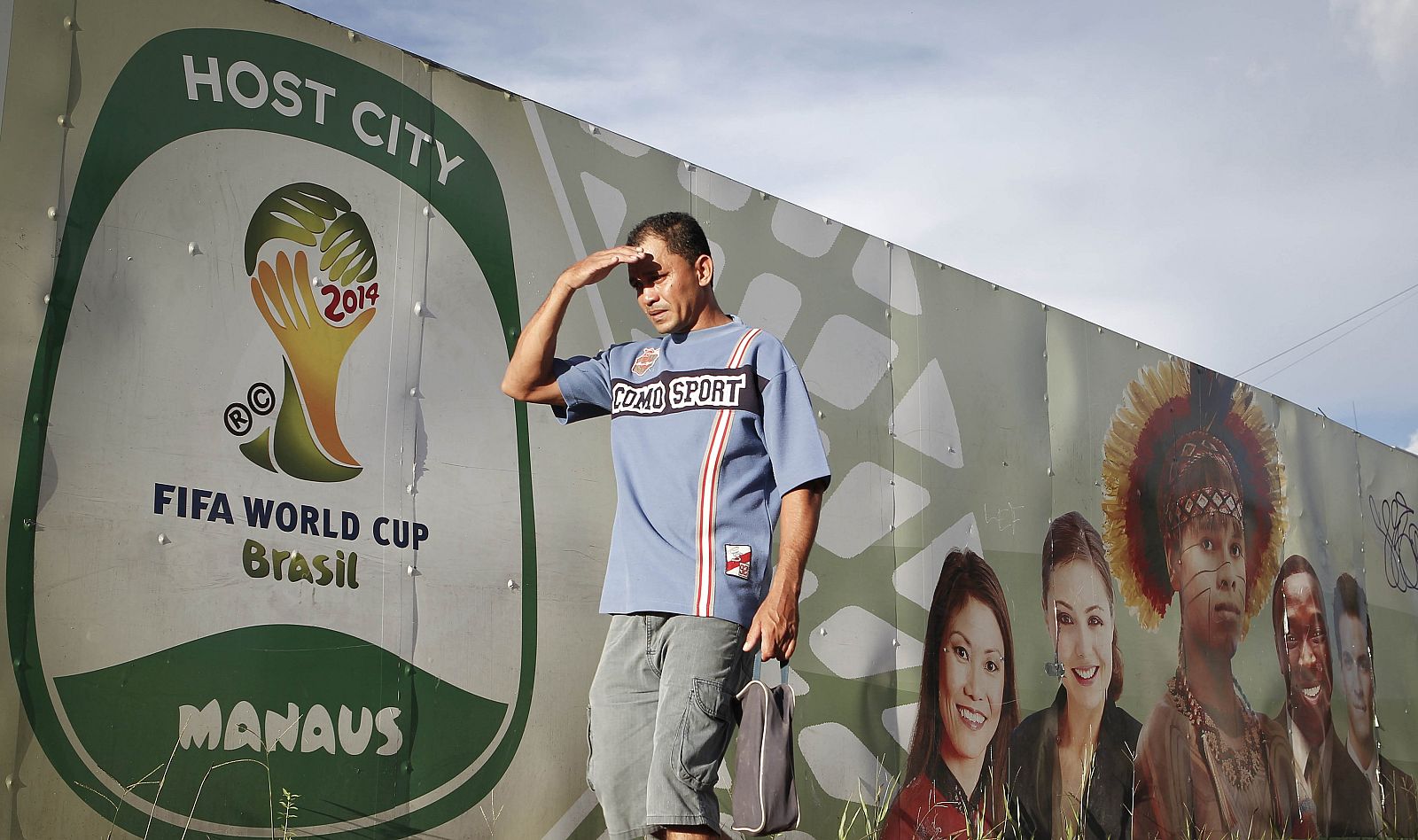 A man walks past a temporary wall surrounding the ongoing construction work at the Arena da Amazonia Stadium in Manaus