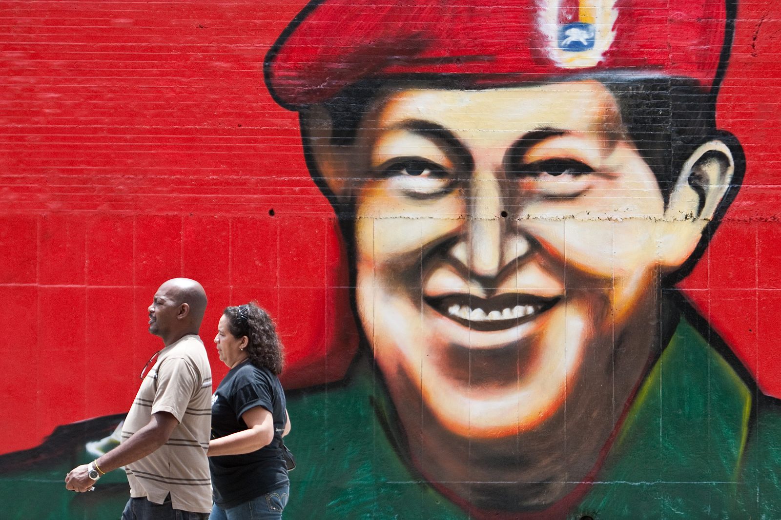 Una pareja camina frente a la imagen pintada del presidente de Venezuela, Hugo Chávez