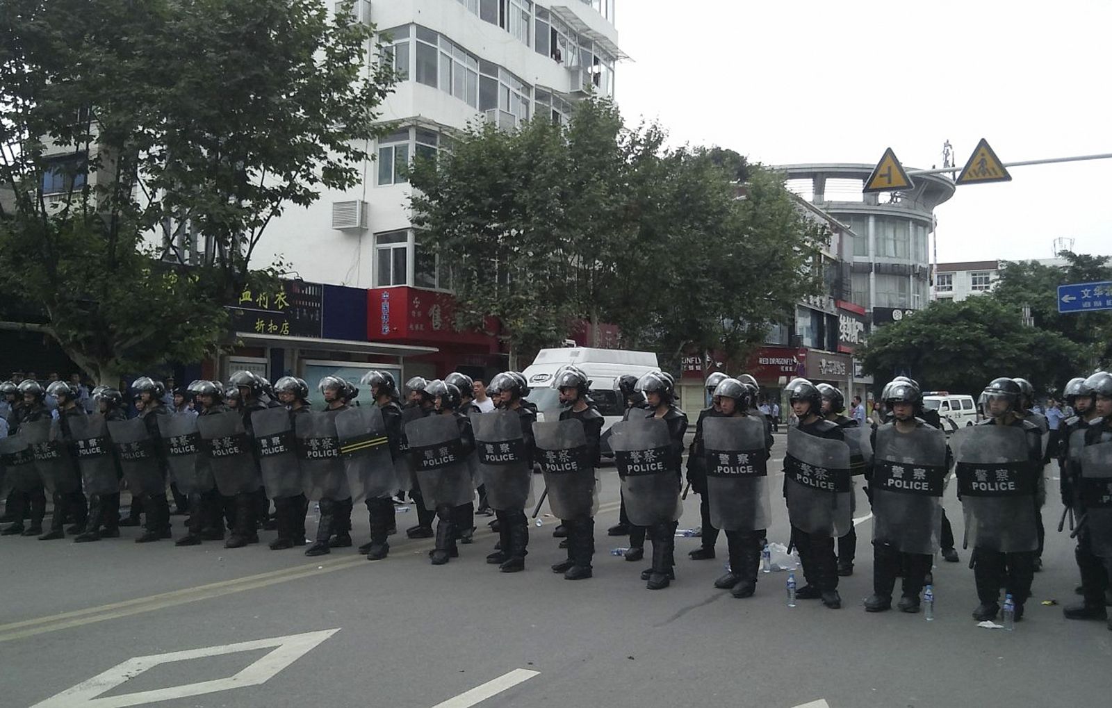 Riot police stand in a line to guard a street during a protest in Shifang