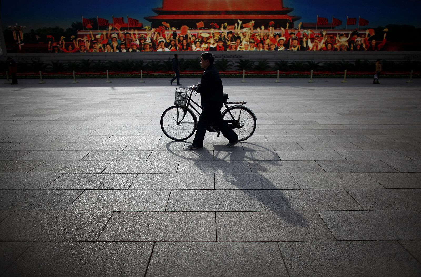 Un hombre pasa con su bicicleta frente a un cartel de propaganda en la Plaza de Tiananmen de Pekín