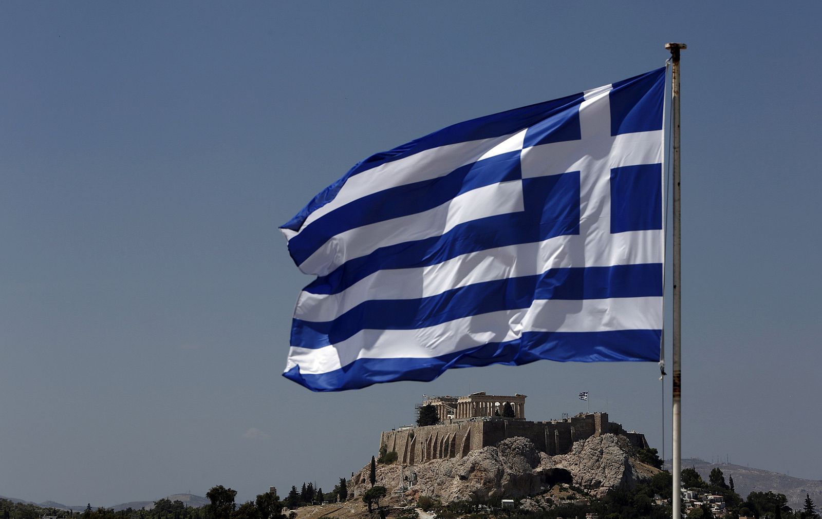 A Greek flag flutters in front of the Acropolis hill in Athens