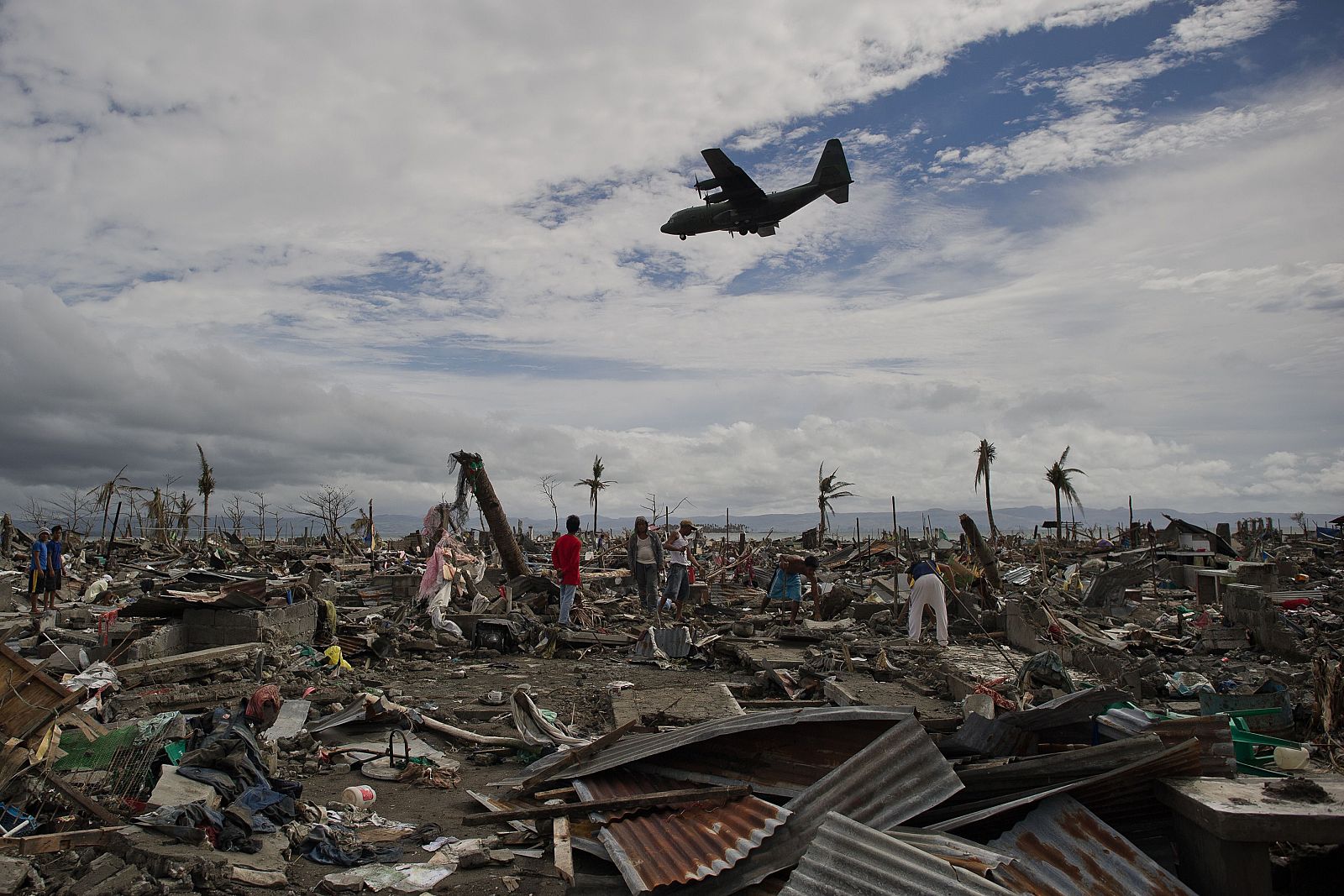 Damnificados del tifón Haiyan, entre las ruinas de sus casas mientras un avión con ayuda se dirige al aeropuerto de Tacloban