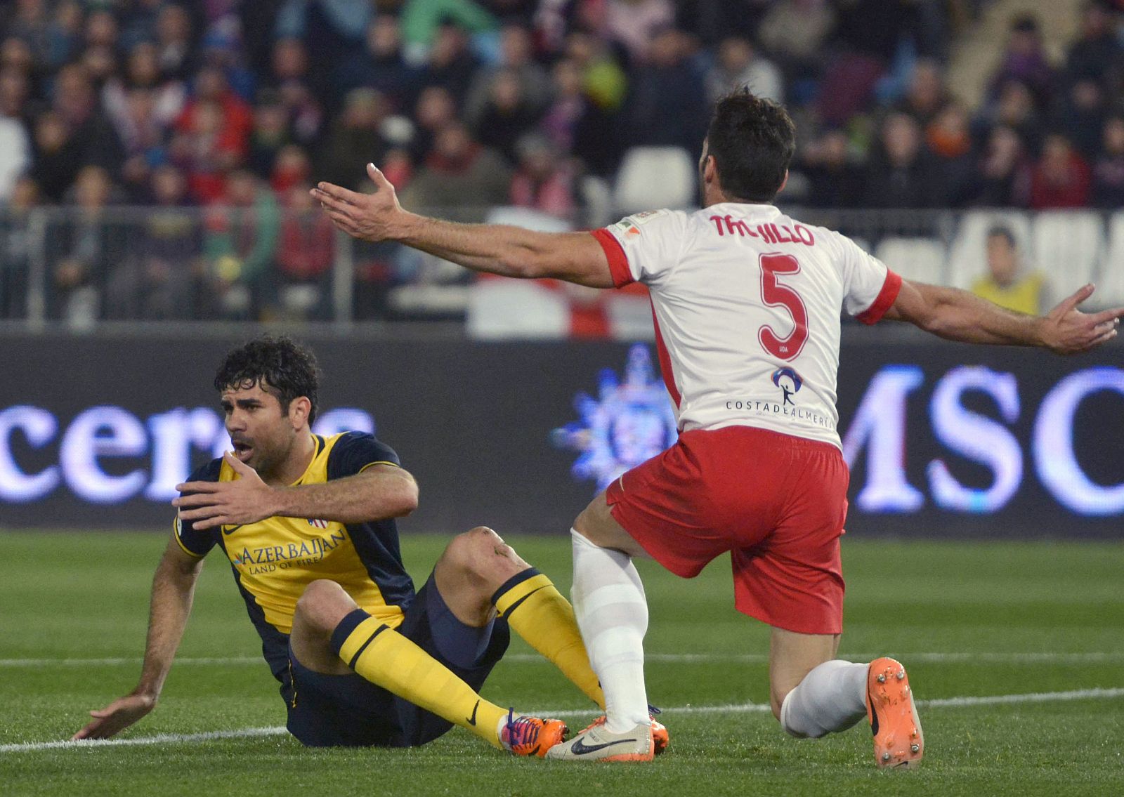 Atletico Madrid's Costa sits on the pitch as Almeria's Trujillo reacts during their soccer match in Almeria