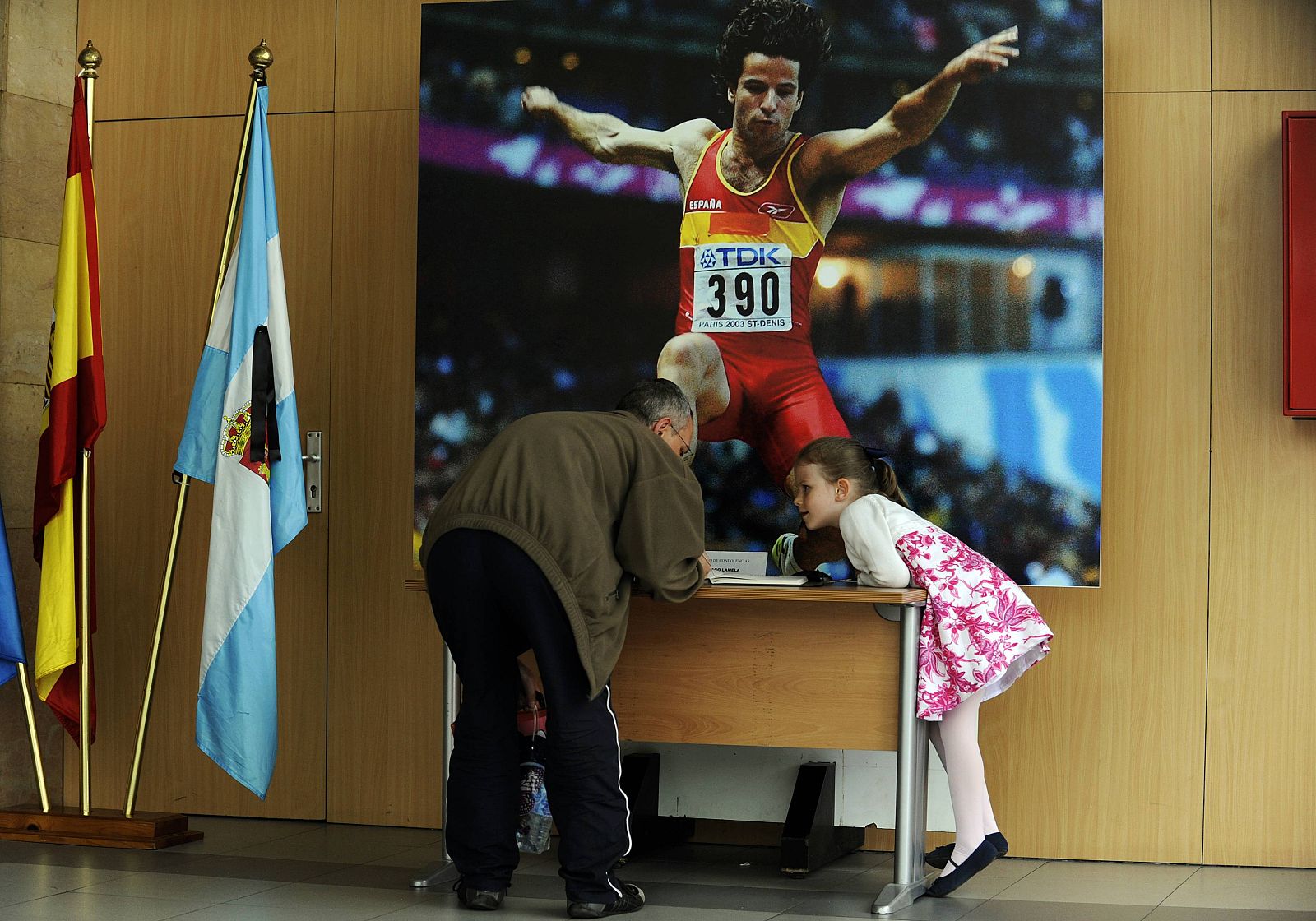 A man and his daughter sign in the book of condolences for former Spanish athlete Yago Lamela at the sports arena where he trained, in Aviles