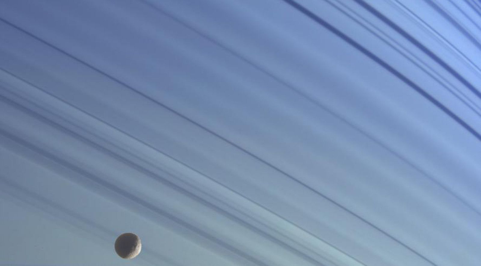 La pequeña luna de hielo Mimas sobre el fondo azul del hemisferio norte de Saturno.