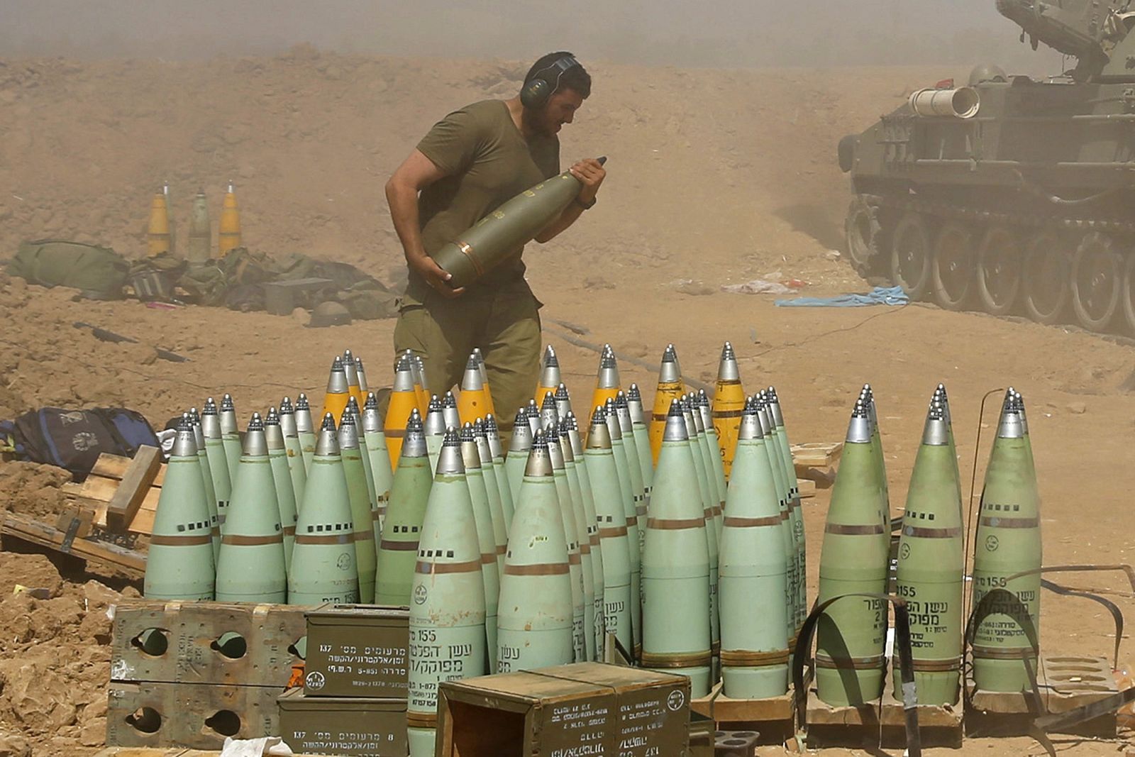 An Israeli soldier carries a shell at a mobile artillery unit while it fires towards the Gaza Strip