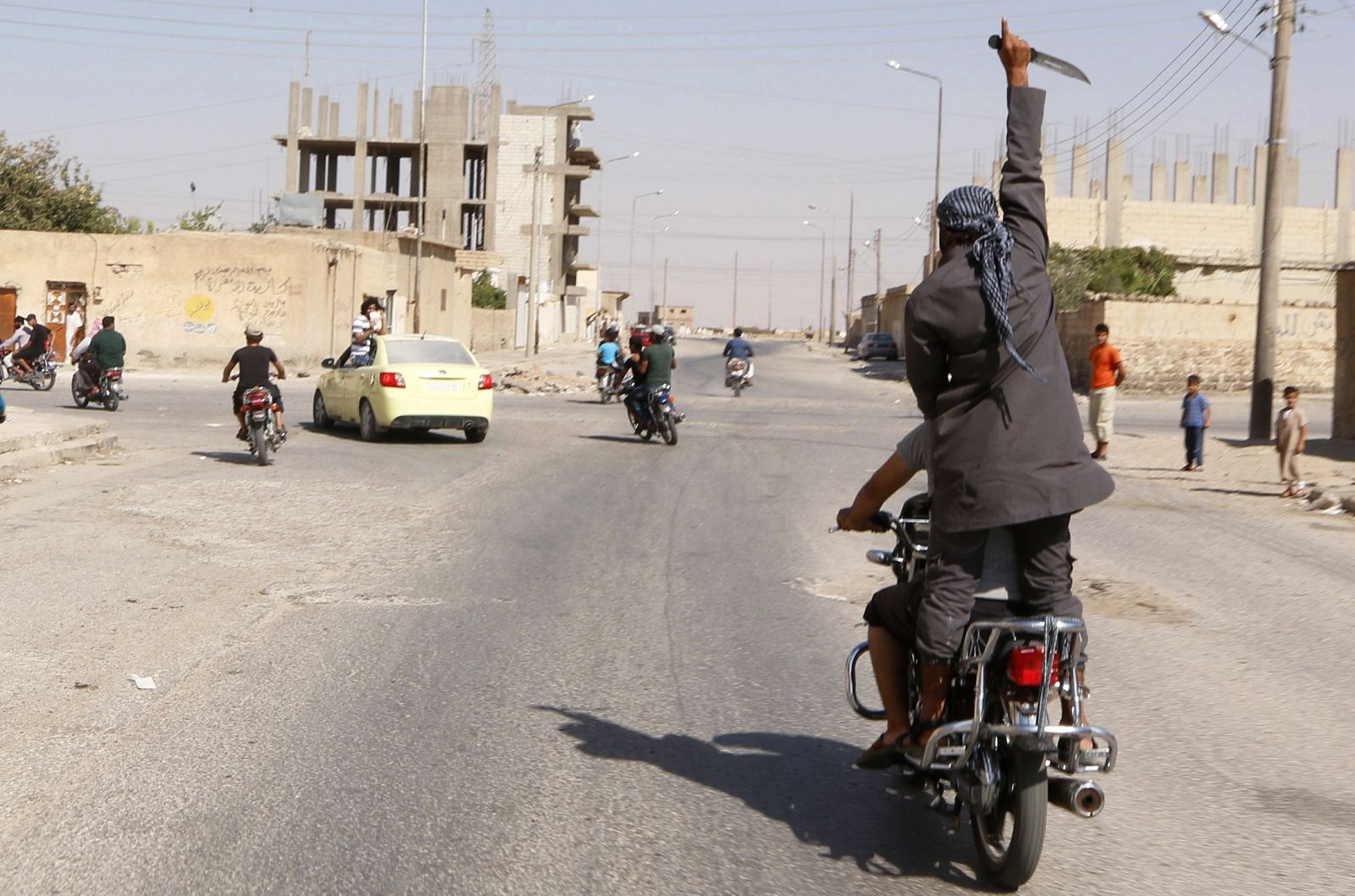 Man holds up a knife as he rides on the back of a motorcycle touring the streets of Tabqa city with others in celebration after Islamic State militants took over Tabqa air base, in nearby Raqqa city