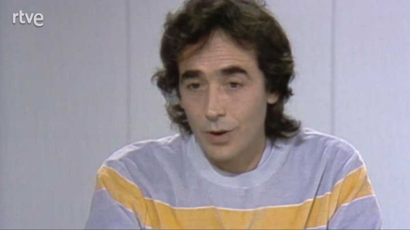 Joan Manuel Serrat, con camiseta gris y amarilla, participa en lo que parece una entrevista televisiva nocturna.  Su expresin denota que est hablando.