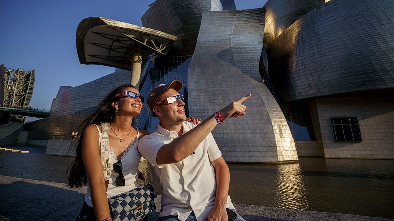 Una pareja observa este miércoles el eclipse solar con el Museo Guggenheim de Bilbao al fondo