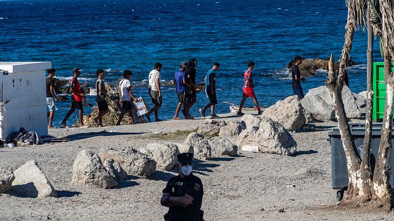 Migrantes hacen cola para recibir una distribución de alimentos de la Cruz Roja en la playa de Trampolín