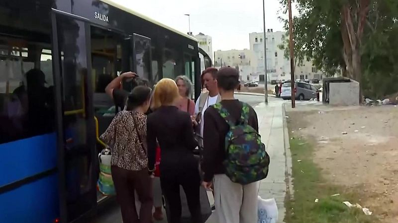 Personas esperan junto a la puerta abierta de un autobús urbano con "SALIDA" escrito. Se aprecian detalles de vestimenta y una mochila de camuflaje.