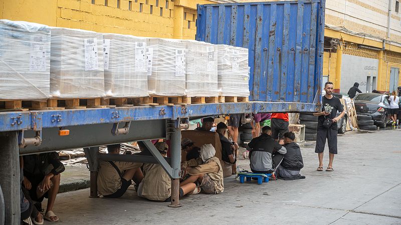 Varios inmigrantes se protegen de la lluvia bajo un camión